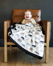 Baby smiling on a chair, wrapped in Safari Blanket featuring animal silhouettes in neutral tones.