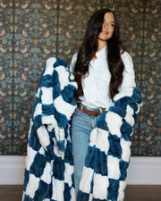 Woman wearing Hugs Check Blue Blanket, showcasing its plush checkered pattern in white and deep navy.