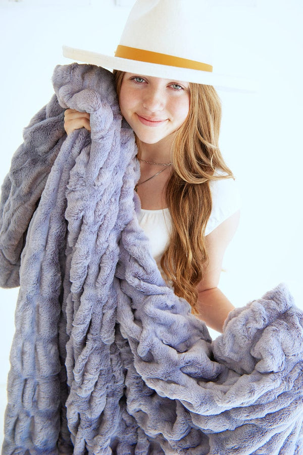 Young woman holding a light purple blanket with gray hues between her arms.
