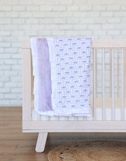 Minky Couture Lilac Ribbon Blanket draped over a crib, featuring purple bows on white with lavender plush backing.
