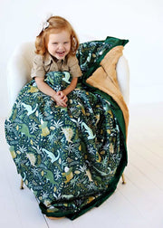 Minky Couture Little Dino Green Blanket featuring colorful dinosaurs with a child happily wrapped in it.