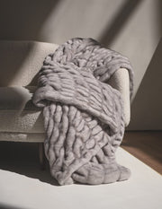 Hugs Chai Blanket draped over a cozy sofa, showcasing its plush texture and soft gray color.