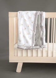 Cozy Shining Stars Blanket draped over a crib, featuring gold and silver star clusters on white, with a plush silver backing.