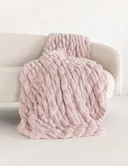 A chunky plush blush pink throw blanket draped over a light beige sofa against a clean white background.