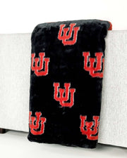 Black plush Minky Couture University of Utah blanket with red U logo draped over light gray sofa arm.