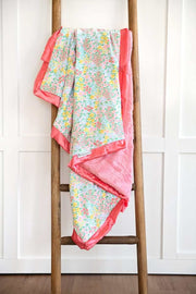 Dainty Floral Pastel Blanket displayed on a wooden ladder, featuring small colorful flowers and a coral satin ruffle.