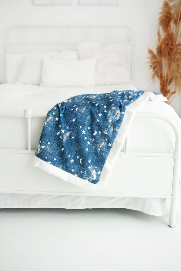 Navy blue blanket with cream stars and moons on it laid over the bottom corner of a bed.