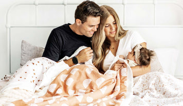 Hospital Bag Checklist – What To Pack in Your Hospital Bag for Childbirth: new parents with their baby on a bed.