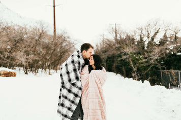 Couple wrapped in cozy blankets in a snowy landscape for Valentine’s Day Gift Guide.