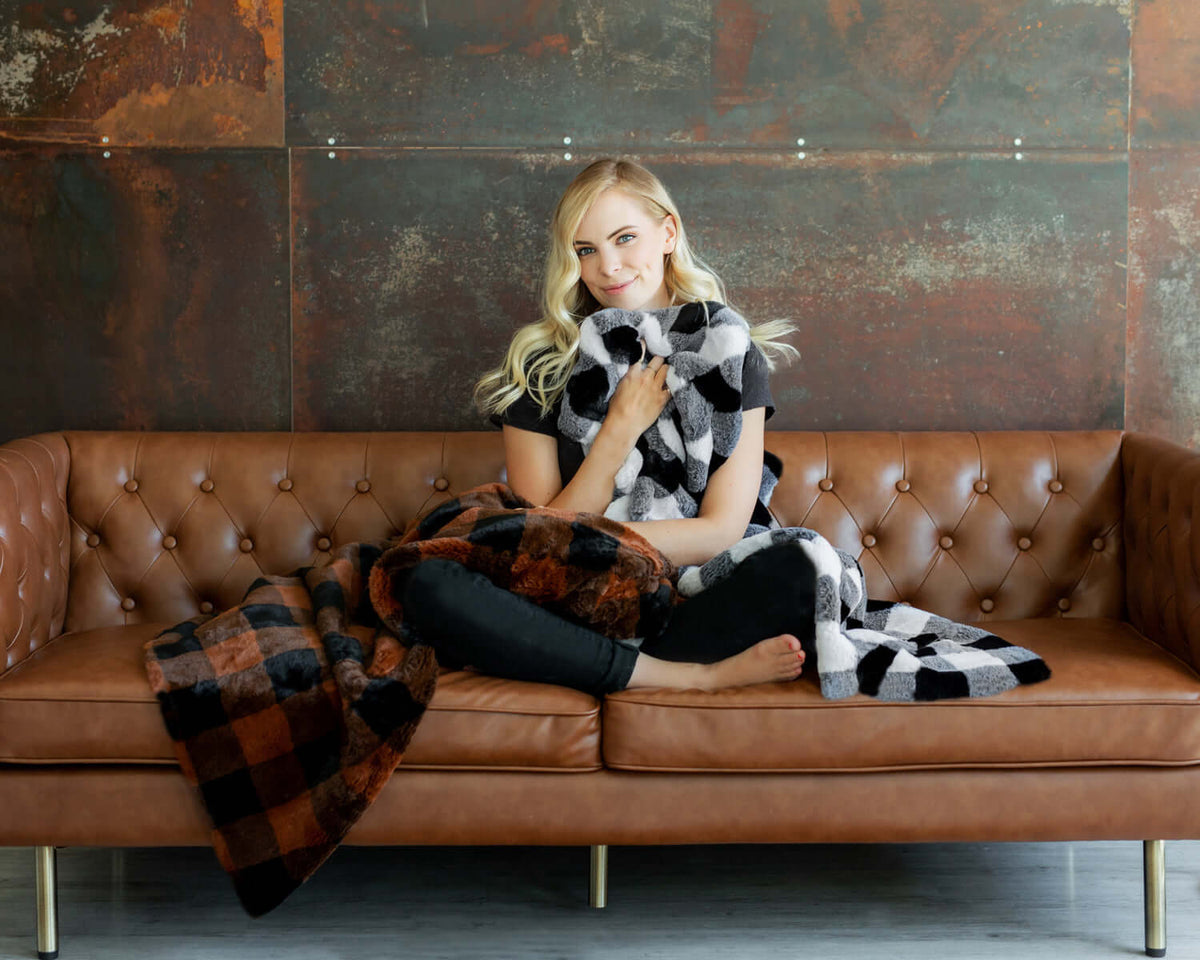 How to Style Your Sofa Like a Pro: Woman wrapping herself in a cozy blanket on a stylish brown leather sofa.