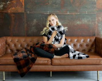 How to Style Your Sofa Like a Pro: Woman wrapping herself in a cozy blanket on a stylish brown leather sofa.