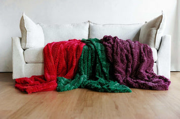 A cozy living room scene featuring a light sofa adorned with vibrant red, green, and purple throw blankets.