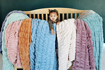 Decoration Inspiration - 12 Baby Nursery Themes to Suit Every Style with a baby among colorful cozy blankets.