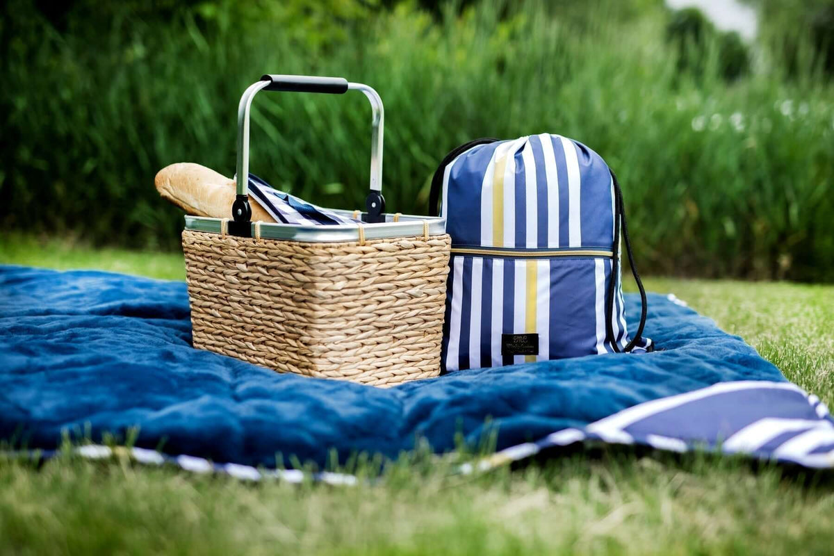 A picnic basket and backpack on a blue blanket in a sunny outdoor setting, Guide to Planning the Perfect Picnic.
