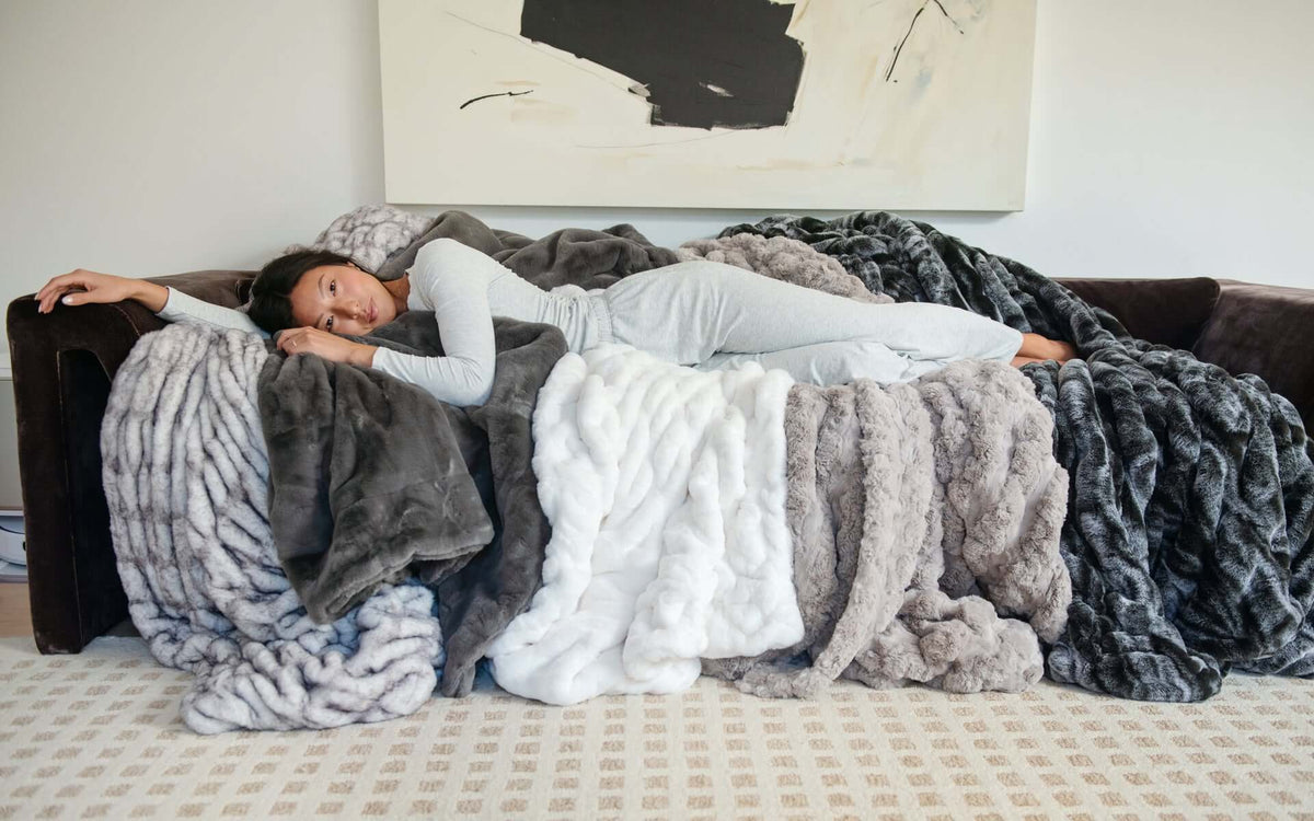 A woman resting comfortably on a couch surrounded by soft, cozy blankets, ideal for creating comforting sympathy gifts.