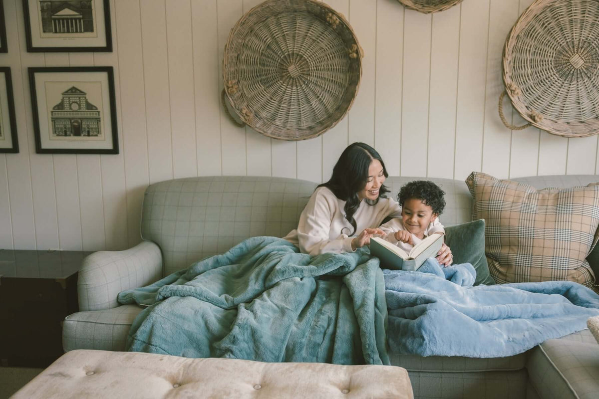 A mother and child reading a book together on a cozy couch, wrapped in soft blankets, showcasing a warm home atmosphere.