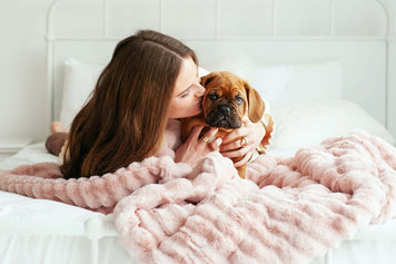Understanding and Managing Pet Anxiety with Anxiety Blankets: woman cuddling a puppy on a bed with a soft blanket.