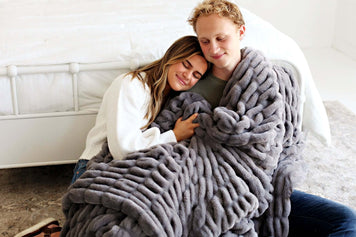 Couple snuggling under a cozy grey blanket, perfect for engagement gift ideas.