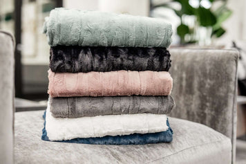 What to do with Old Blankets - stacked old blankets in various colors on a sofa.