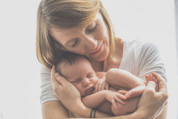 Mom celebrating monthly baby milestones with her sleeping baby in her arms, Get Snap Happy With These 16 Creative Ways to Celebrate Monthly Baby Milestones.