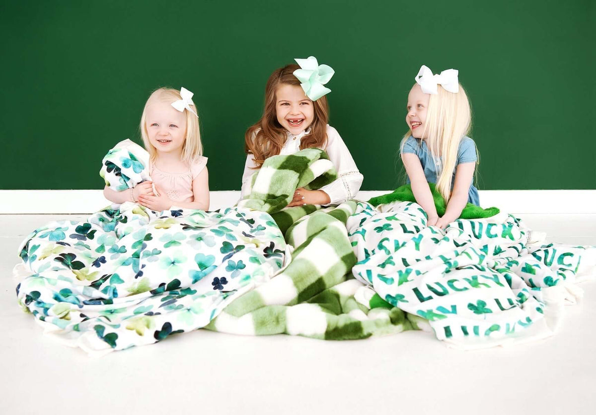 Don't Get Caught in a Pinch! Three girls smiling with St. Patrick's Day green blankets, celebrating the holiday spirit.