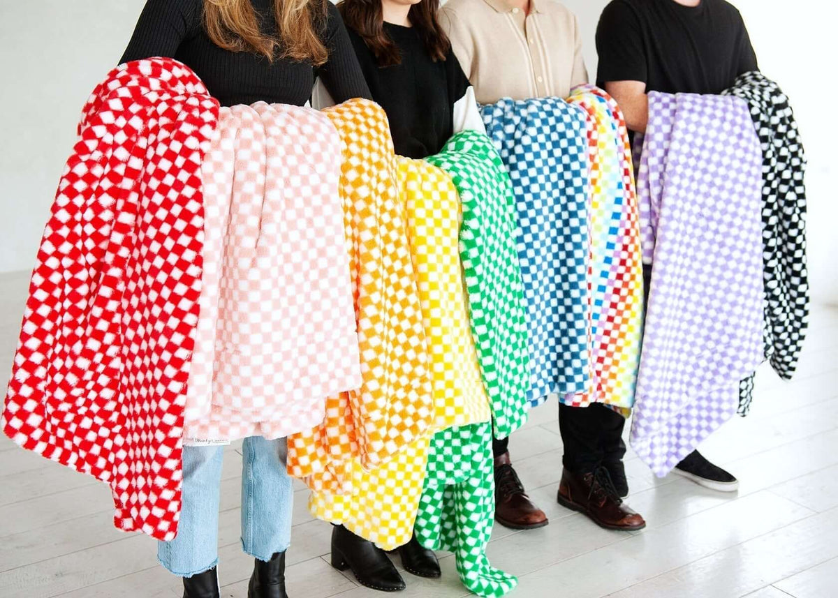 Colorful checkered blankets held by four models, showcasing a variety of vibrant patterns and textures.