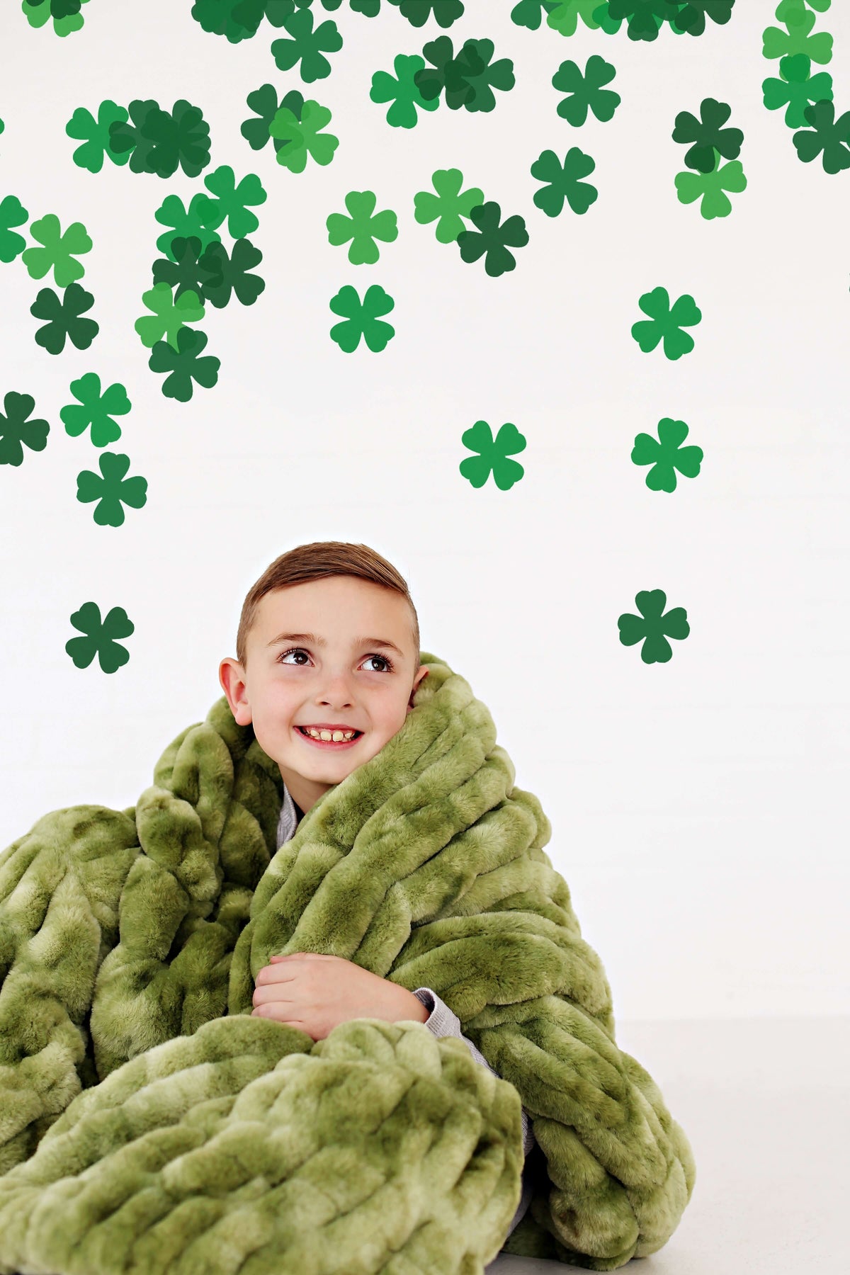 6 Blankets You Need For St. Patrick's Day 🍀 To Stay Pinch-Free: A child cozy in a green blanket with shamrock decorations.