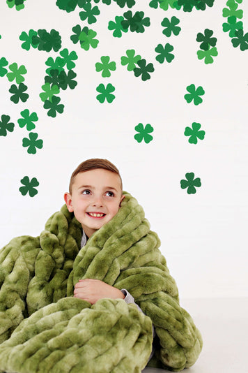 6 Blankets You Need For St. Patrick's Day 🍀 To Stay Pinch-Free: A child cozy in a green blanket with shamrock decorations.