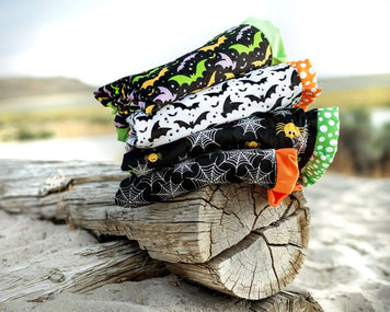 Colorful Halloween blankets in bat and spider patterns stacked on a log outdoors.