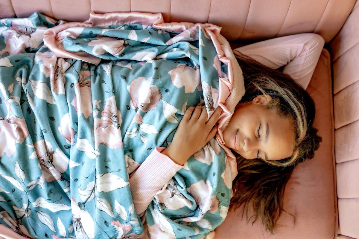 A young woman sleeping comfortably on a couch, wrapped in a floral blanket, illustrating what your sleeping position says about you.
