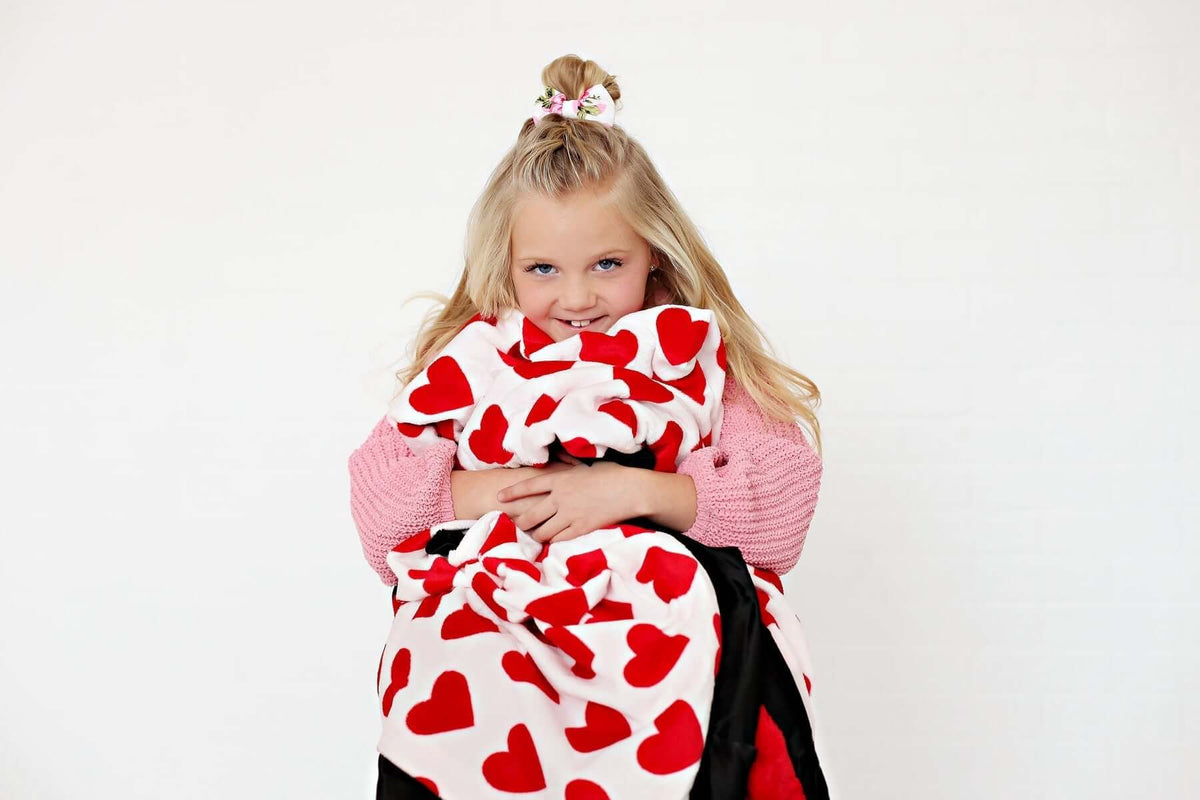 A girl with a ponytail holding a blanket covered in red hearts, enjoying a cozy moment.
