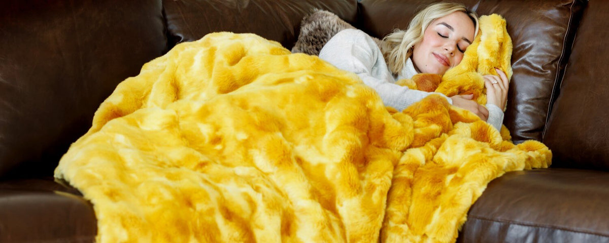 A woman relaxed under a Minky Couture faux fur blanket, highlighting the benefits of calming blankets for sleep and relaxation.