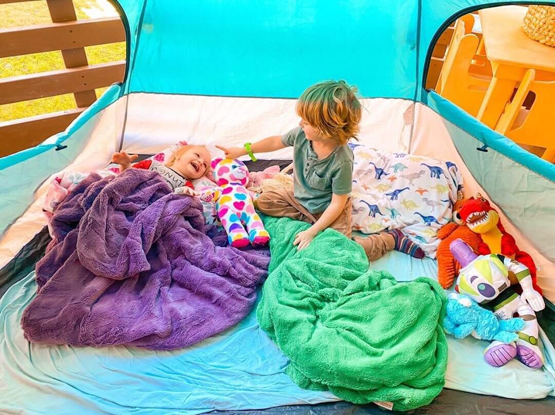Fun Blanket Fort Ideas to Make With Your Kids: Children playing in a colorful fort with blankets and toys.