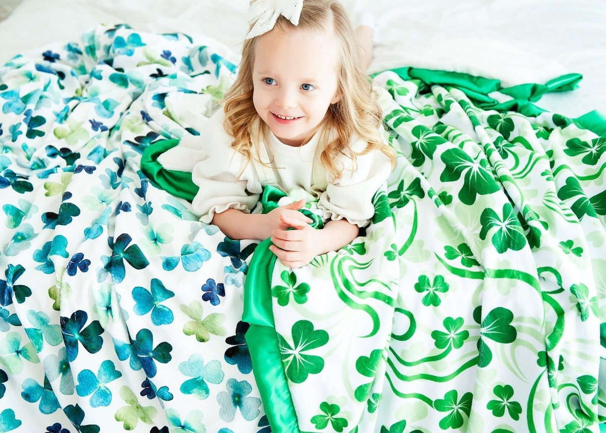 A girl smiling under a colorful shamrock blanket, perfect for celebrating St. Patrick's Day and learning how to catch a Leprechaun!