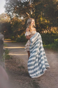 Model holding the Hugs French Stripe Blanket with blue stripes in a natural outdoor setting.