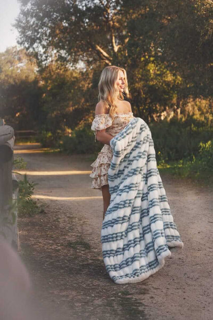 Model holding the Hugs French Stripe Blanket with blue stripes in a natural outdoor setting.