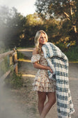 A smiling woman wearing a floral dress holds the Hugs French Stripe Blanket on a sunlit outdoor path.