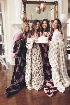 Four women holding a cake, wrapped in plush Minky Couture blankets.