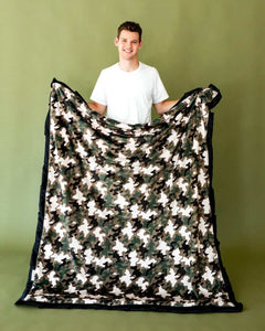 A person holding a Camo Blanket featuring a stylish camouflage pattern and plush black edges.