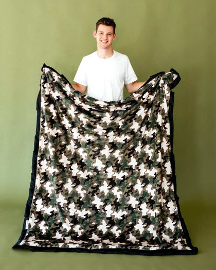 A person holding a Camo Blanket featuring a stylish camouflage pattern and plush black edges.
