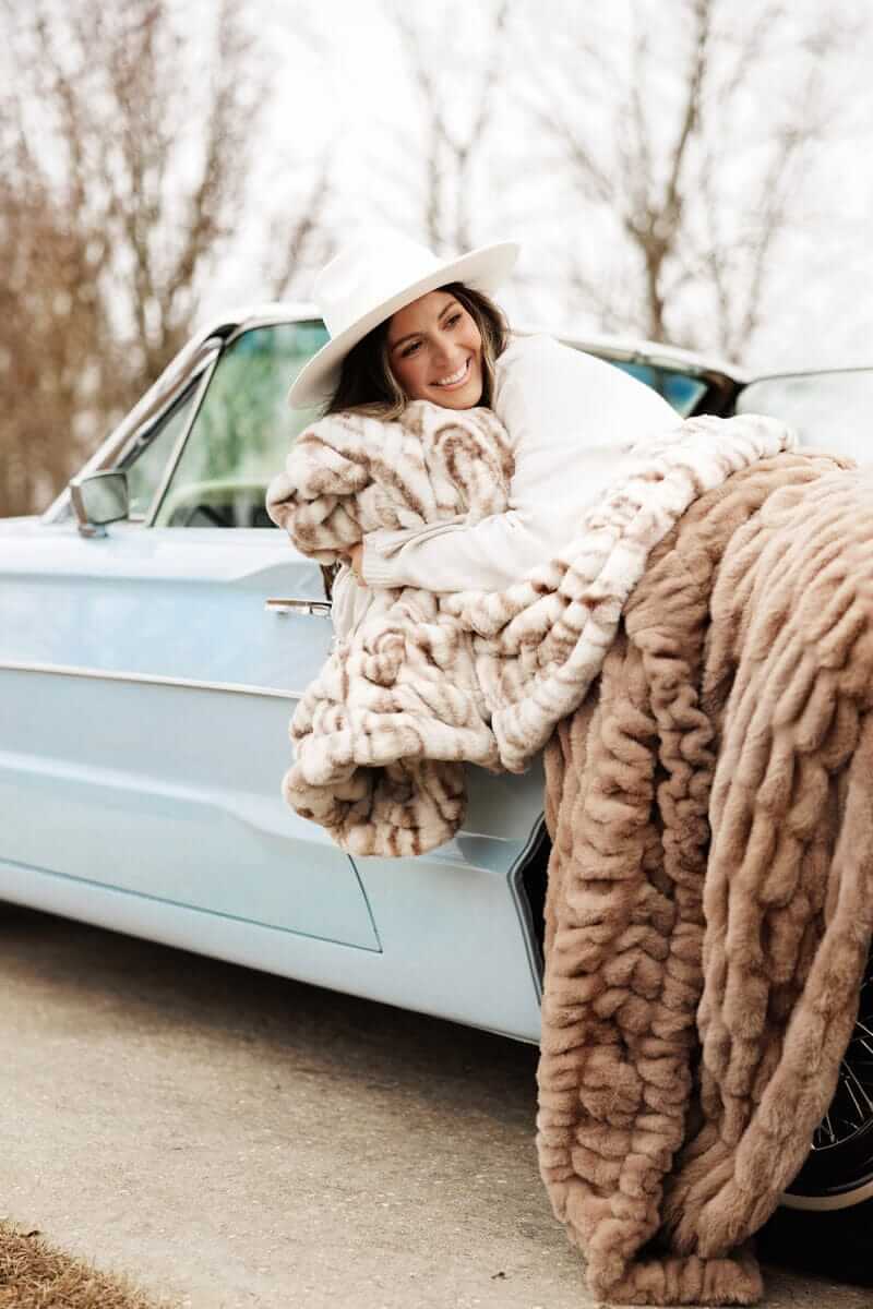 Woman smiling in a vintage car, wrapped in a plush Hugs Kaci Chocolate Marble blanket.