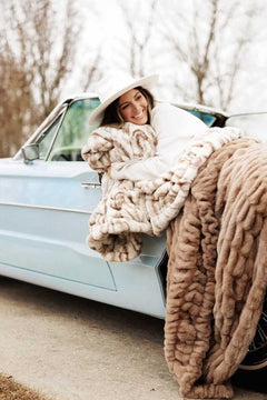 Woman smiling in a vintage car, wrapped in a plush Hugs Kaci Chocolate Marble blanket.