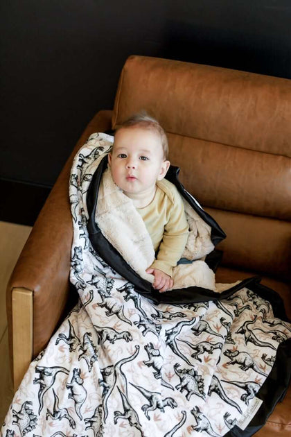 Child snuggled in a Big Dino Blanket featuring black and tan dinosaurs, perfect for cozying up in style.