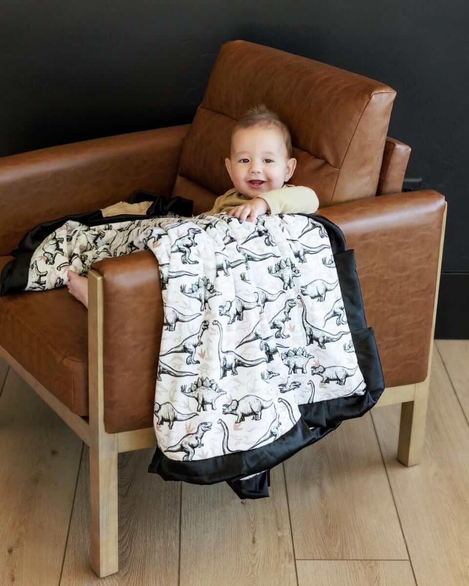 Baby enjoying the Big Dino Blanket featuring black and tan dinosaurs on a cozy white background.
