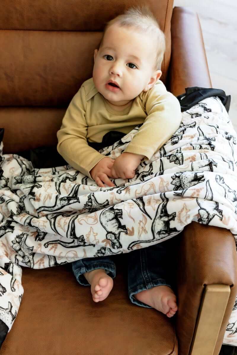 Baby wrapped in Big Dino Blanket featuring black and tan dinosaurs on a white background.