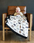 Baby smiling on a chair, wrapped in Safari Blanket featuring animal silhouettes in neutral tones.