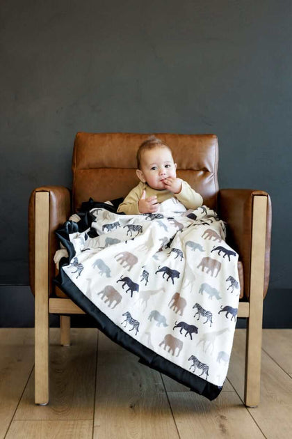 Baby wrapped in Safari Blanket featuring animal silhouettes, sitting on a chair.