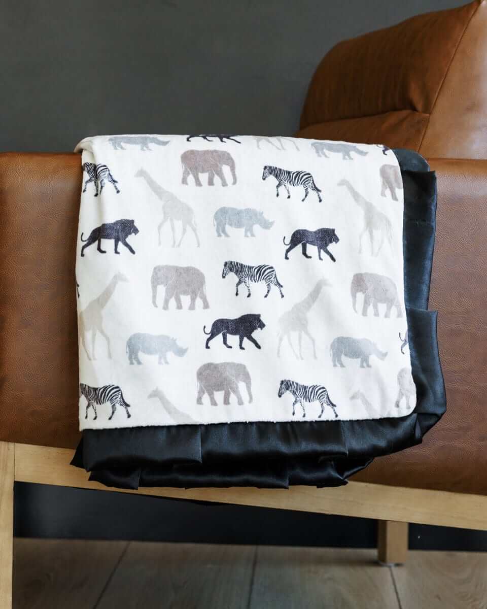 Safari Blanket with animal silhouettes on white background, featuring a black satin ruffle and plush backing.