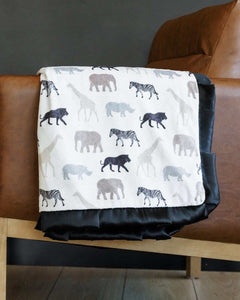 Safari Blanket with animal silhouettes on white background, featuring a black satin ruffle and plush backing.