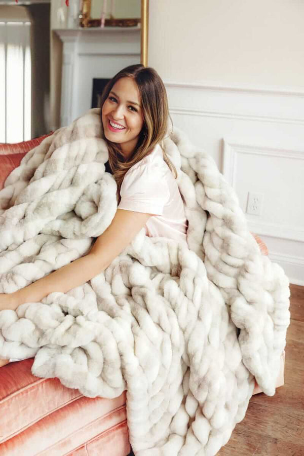 Woman smiling while wrapped in a faux fur Minky Couture blanket on a sofa.